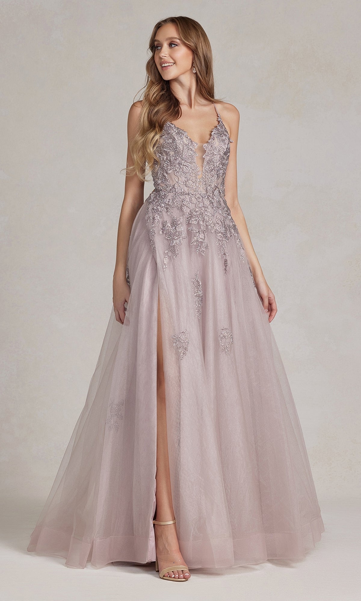 A woman in an open-back long prom ball gown with beads, featuring a sleeveless design, deep V neckline, tulle skirt, high slit, and beaded lace appliques stands against a neutral background.
